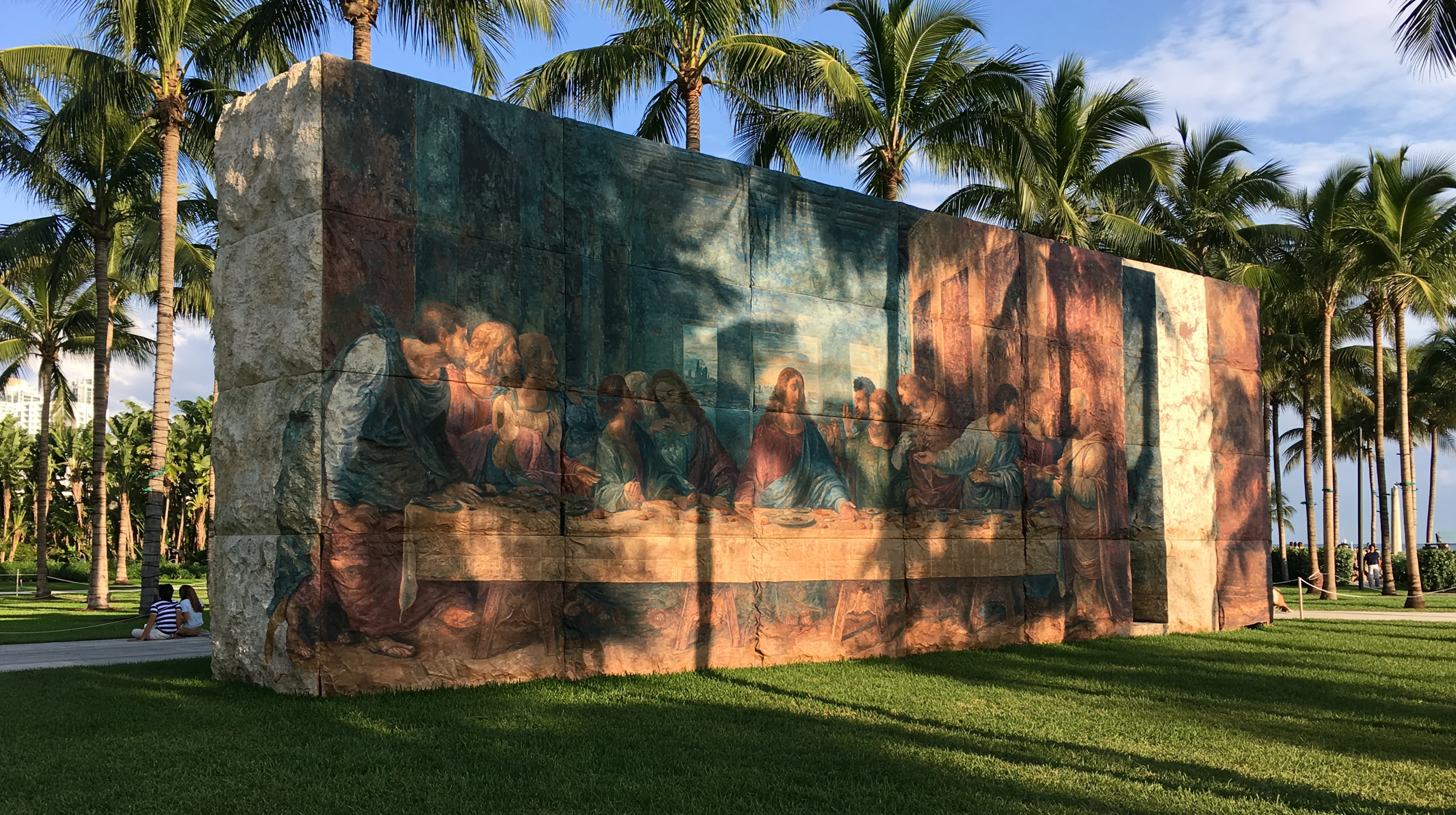 A Last Supper relief on a stone block under palms in Miami sunlight